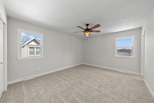 carpeted spare room with visible vents, plenty of natural light, and ceiling fan