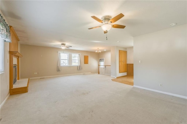 unfurnished living room featuring baseboards, light colored carpet, a glass covered fireplace, and ceiling fan with notable chandelier