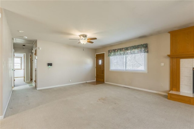 unfurnished living room with a tiled fireplace, light colored carpet, baseboards, and a ceiling fan