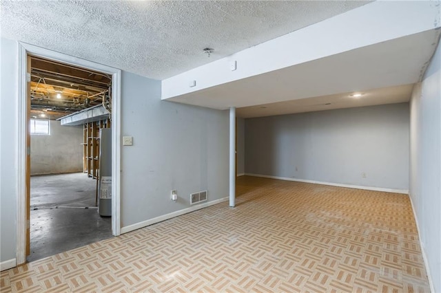 basement featuring water heater, visible vents, a textured ceiling, and baseboards