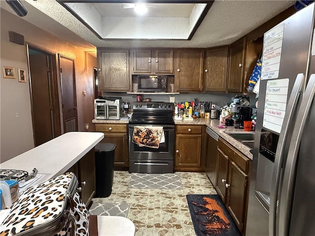 kitchen with black appliances, light countertops, stone finish floor, a textured ceiling, and a raised ceiling