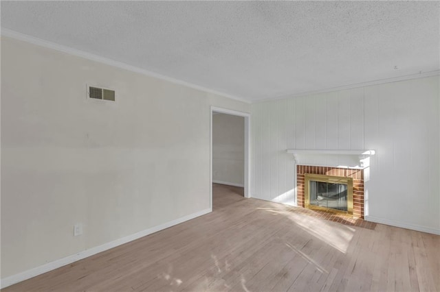 unfurnished living room with wood finished floors, crown molding, a fireplace, and visible vents