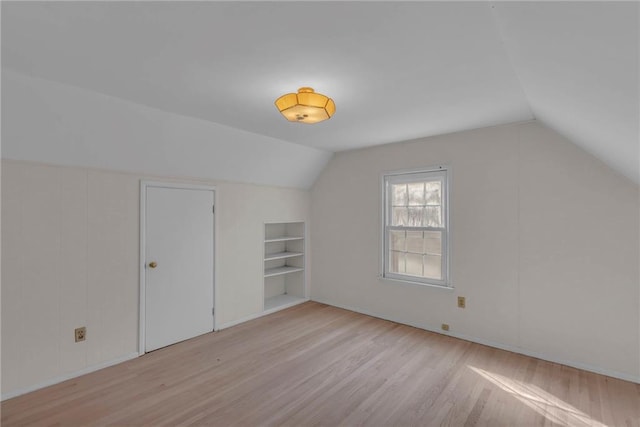 additional living space featuring vaulted ceiling, built in features, and wood finished floors