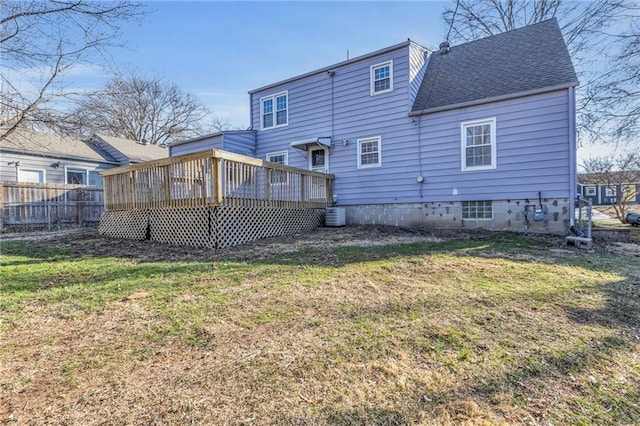 rear view of house with a yard, roof with shingles, a wooden deck, and fence