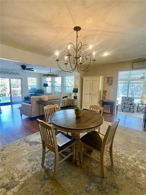 dining room with ceiling fan with notable chandelier, plenty of natural light, wood finished floors, and a textured ceiling