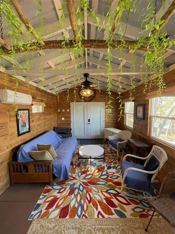 living area with a wall mounted air conditioner, wooden walls, vaulted ceiling with beams, and ceiling fan