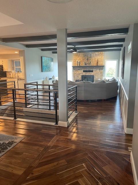 interior space featuring beamed ceiling, a textured ceiling, a stone fireplace, baseboards, and parquet flooring