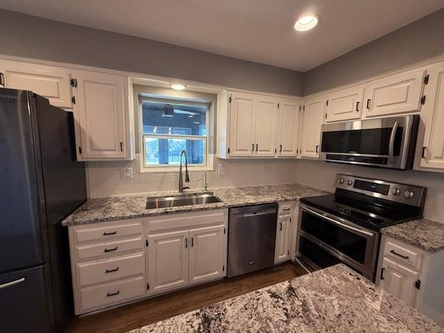 kitchen with a sink, stainless steel appliances, light stone counters, and white cabinets