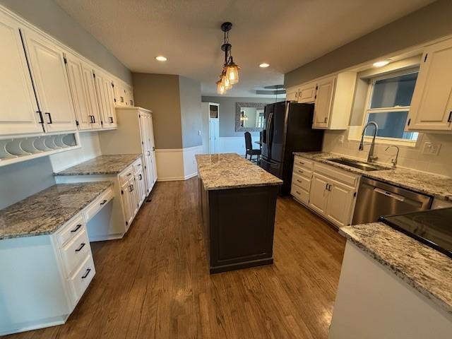 kitchen featuring a sink, a kitchen island, stainless steel dishwasher, white cabinetry, and freestanding refrigerator