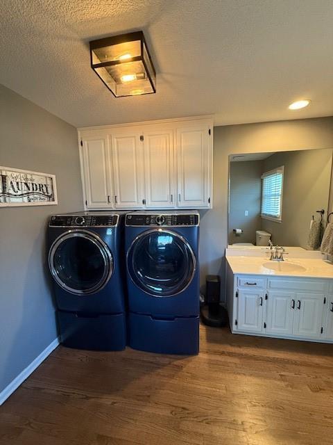 laundry area featuring a sink, dark wood-style floors, cabinet space, separate washer and dryer, and baseboards