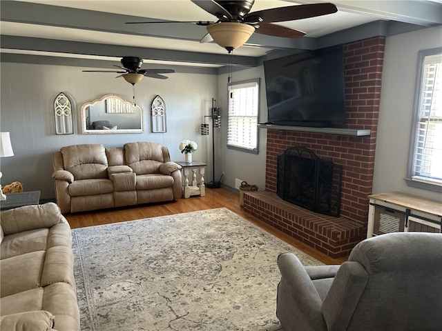 living room featuring beamed ceiling, a brick fireplace, a ceiling fan, and wood finished floors