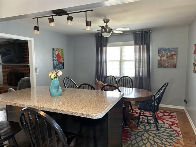 kitchen with a kitchen bar, a ceiling fan, dark wood finished floors, baseboards, and a brick fireplace