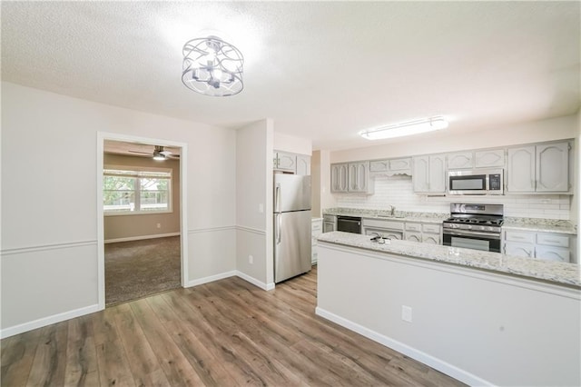 kitchen with wood finished floors, baseboards, a sink, decorative backsplash, and appliances with stainless steel finishes