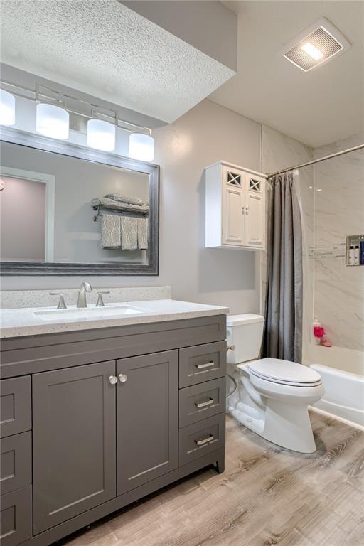 full bathroom featuring visible vents, toilet, wood finished floors, vanity, and shower / bathtub combination with curtain