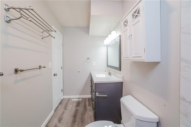 bathroom featuring baseboards, toilet, wood finished floors, and vanity