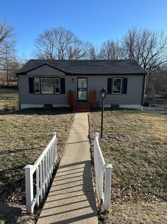 ranch-style home with a front yard, fence, and a shingled roof