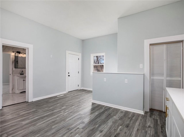 unfurnished living room featuring a sink, baseboards, and dark wood finished floors