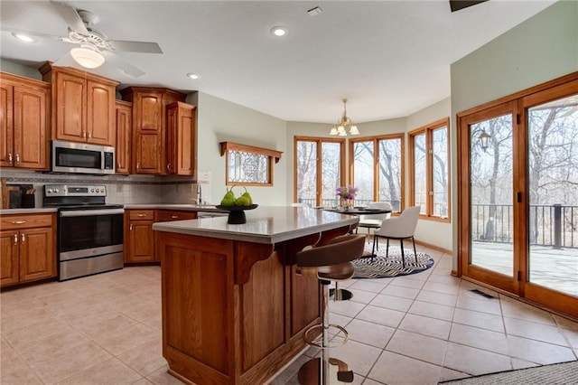 kitchen with light tile patterned floors, decorative backsplash, brown cabinets, a kitchen breakfast bar, and stainless steel appliances