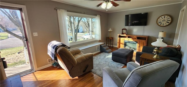 living area featuring wood finished floors, crown molding, a ceiling fan, and baseboards