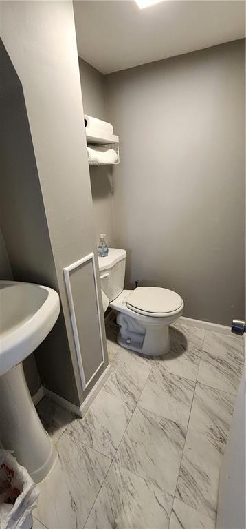 bathroom with toilet, baseboards, and marble finish floor