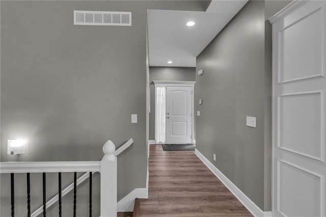 hall featuring wood finished floors, baseboards, visible vents, recessed lighting, and an upstairs landing