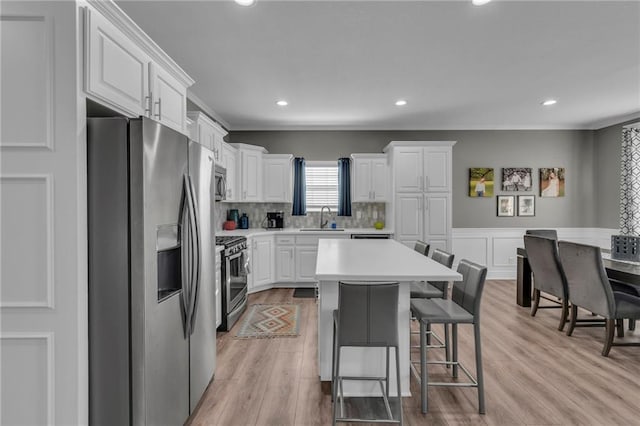 kitchen featuring a sink, stainless steel appliances, light countertops, white cabinets, and a kitchen breakfast bar