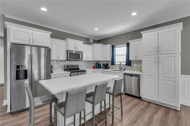 kitchen with a kitchen bar, a sink, white cabinetry, appliances with stainless steel finishes, and light wood finished floors