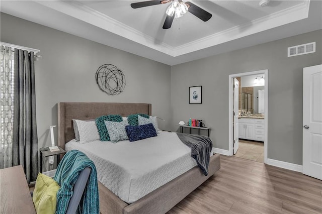 bedroom with visible vents, baseboards, light wood-type flooring, a tray ceiling, and ornamental molding