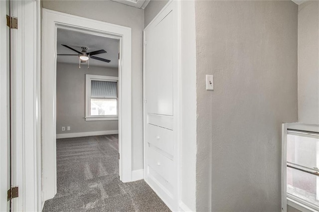 hallway with baseboards, dark colored carpet, and a textured wall