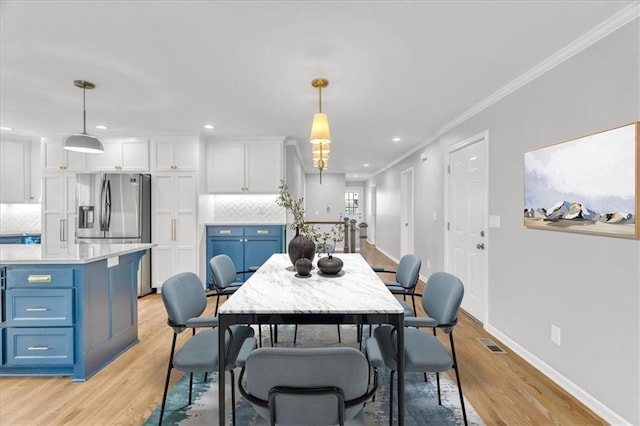 dining room featuring visible vents, baseboards, crown molding, and light wood finished floors