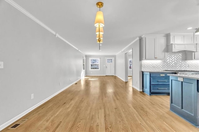 unfurnished living room featuring visible vents, baseboards, light wood-style floors, and crown molding