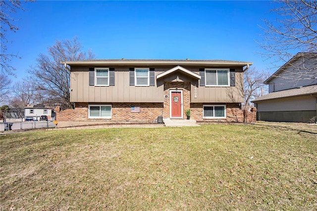 bi-level home featuring brick siding, board and batten siding, a front yard, and fence