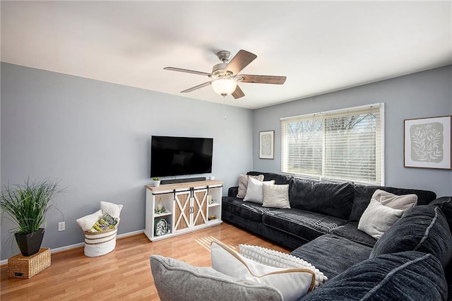 living area with baseboards, a ceiling fan, and light wood finished floors