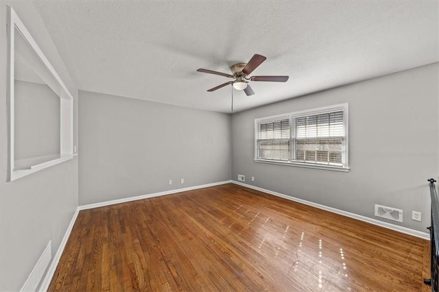 spare room with visible vents, baseboards, wood finished floors, a textured ceiling, and a ceiling fan