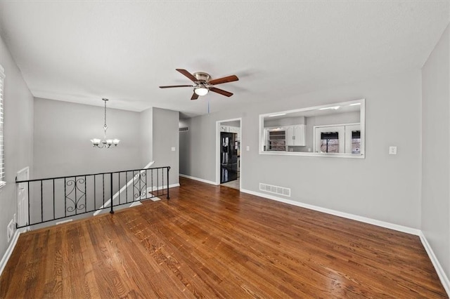 empty room featuring visible vents, ceiling fan with notable chandelier, baseboards, and wood finished floors