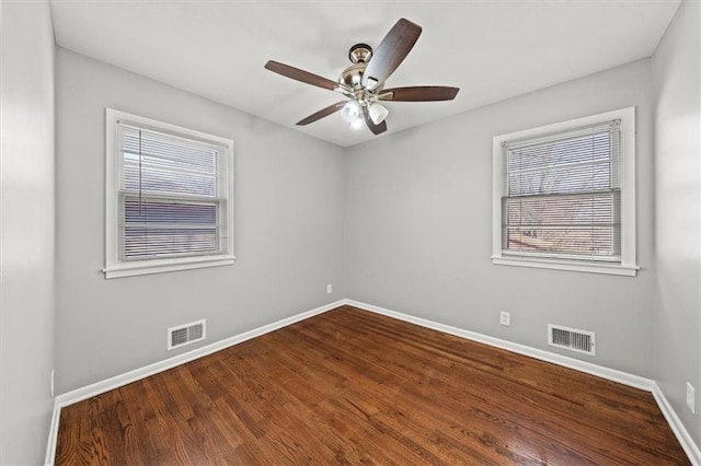 spare room with dark wood finished floors, visible vents, a ceiling fan, and baseboards