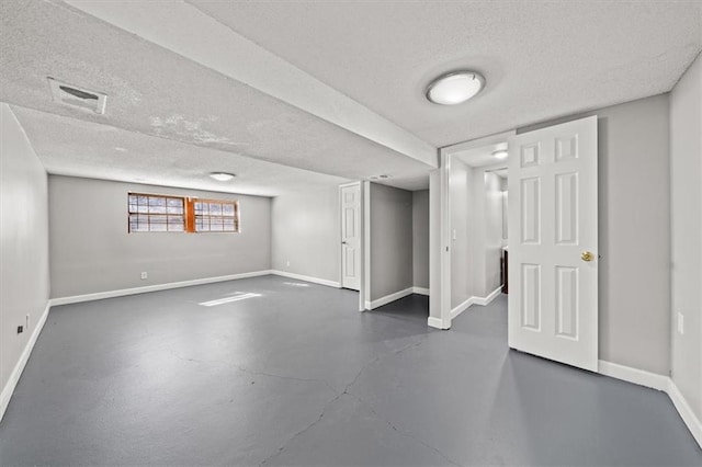 basement featuring visible vents, a textured ceiling, and baseboards