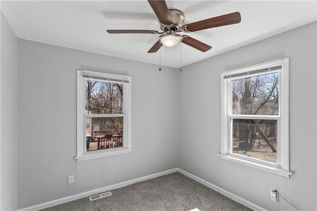 carpeted empty room featuring a wealth of natural light, visible vents, baseboards, and a ceiling fan