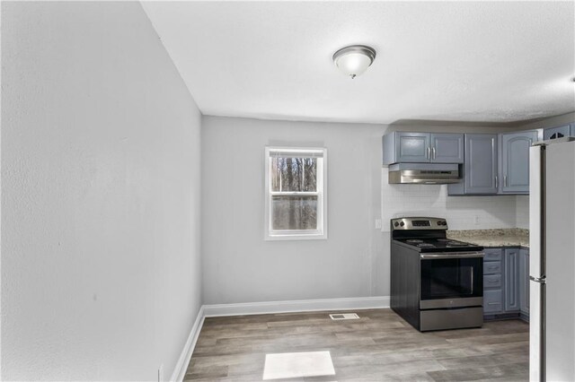 kitchen with under cabinet range hood, freestanding refrigerator, stainless steel range with electric cooktop, light wood-style floors, and decorative backsplash