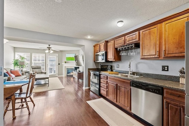 kitchen with a sink, dark countertops, open floor plan, dark wood finished floors, and stainless steel appliances