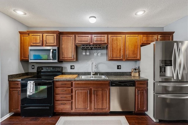 kitchen featuring wood finish floors, brown cabinets, appliances with stainless steel finishes, a textured ceiling, and a sink