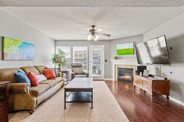 living area with wood finished floors, a ceiling fan, baseboards, a tile fireplace, and a textured ceiling