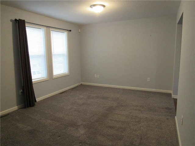 unfurnished room with baseboards and dark colored carpet