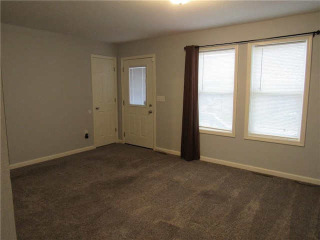 spare room featuring dark carpet and baseboards