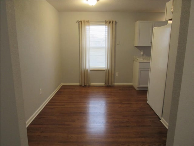 unfurnished dining area featuring dark wood-style floors and baseboards