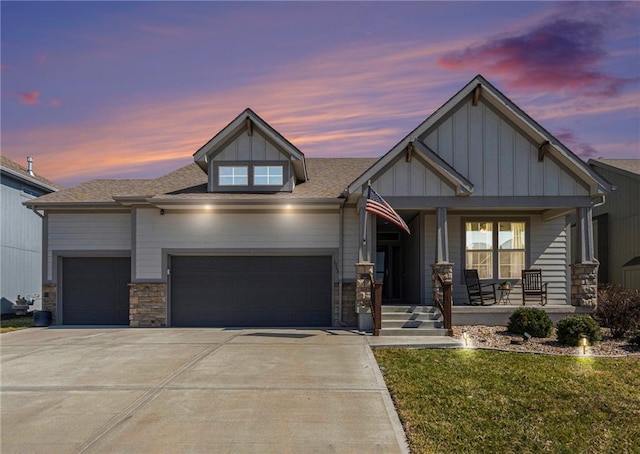 view of front of house featuring board and batten siding, covered porch, driveway, stone siding, and an attached garage