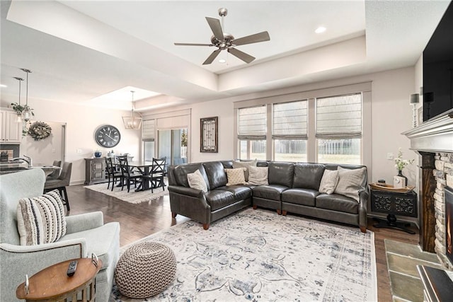 living room featuring a raised ceiling, wood finished floors, a fireplace, baseboards, and ceiling fan