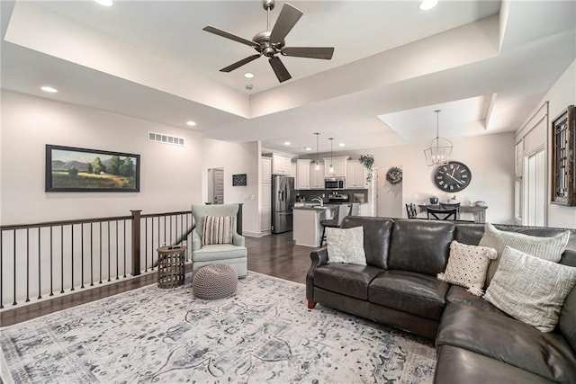 living room featuring visible vents, ceiling fan with notable chandelier, dark wood finished floors, recessed lighting, and a raised ceiling