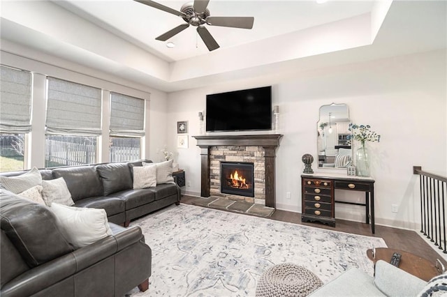 living area with a stone fireplace, baseboards, a tray ceiling, and wood finished floors