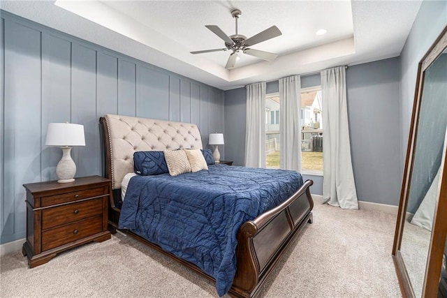 bedroom featuring a raised ceiling, light colored carpet, baseboards, and ceiling fan